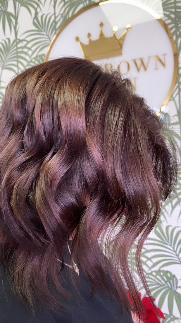 Burgundy balayage waves styled at The Crown Salon in front of the crown sign
